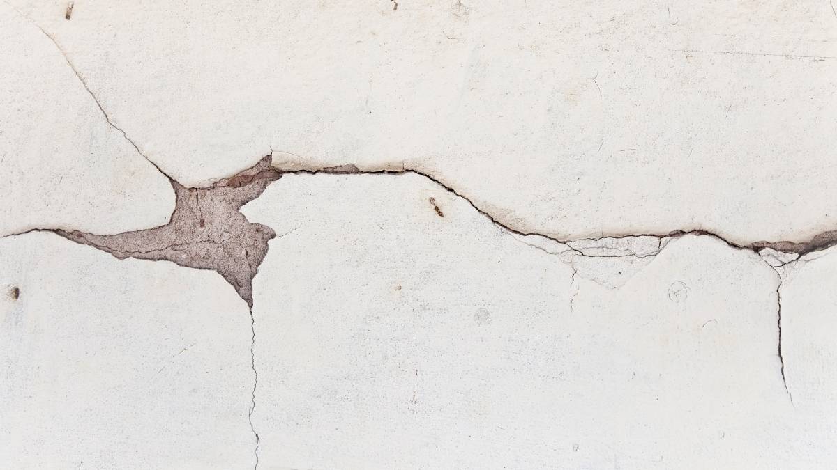 Cracked white plaster wall with horizontal and vertical fissures, revealing underlying brown material.

The texture and imperfections suggest age and decay.